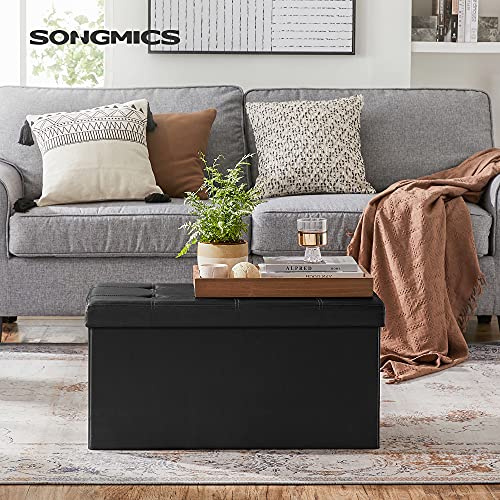 Taburete como mesita o reposapiés frente al sofa con almacenaje para libros, los mandos de la tele o para la mantita de 80 litros de capacidad y con acabado de pvc negro. LSF105 de Songmic