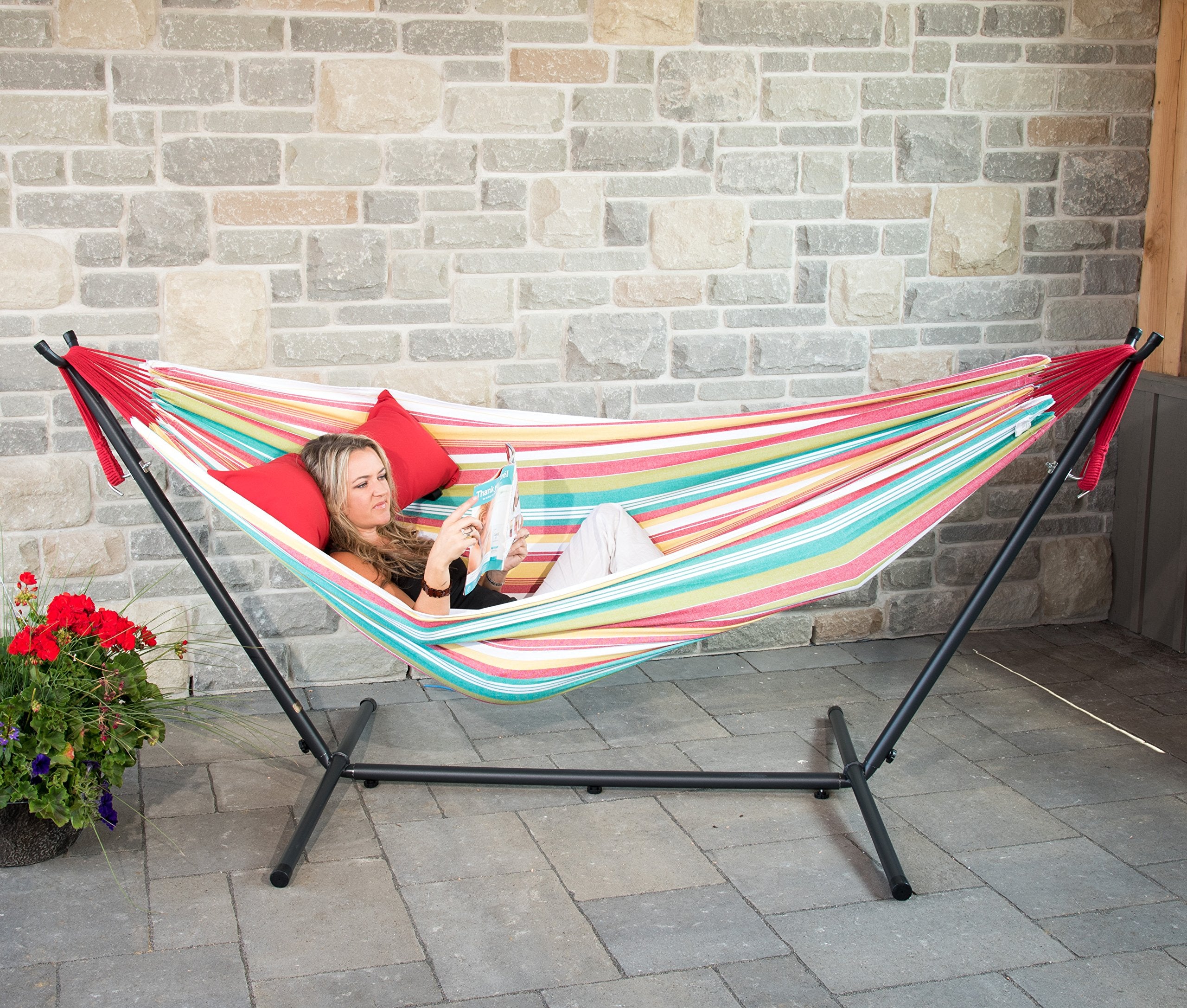 Mujer joven descansando en hamaca Vivere a rayas de colores con estructura en patio